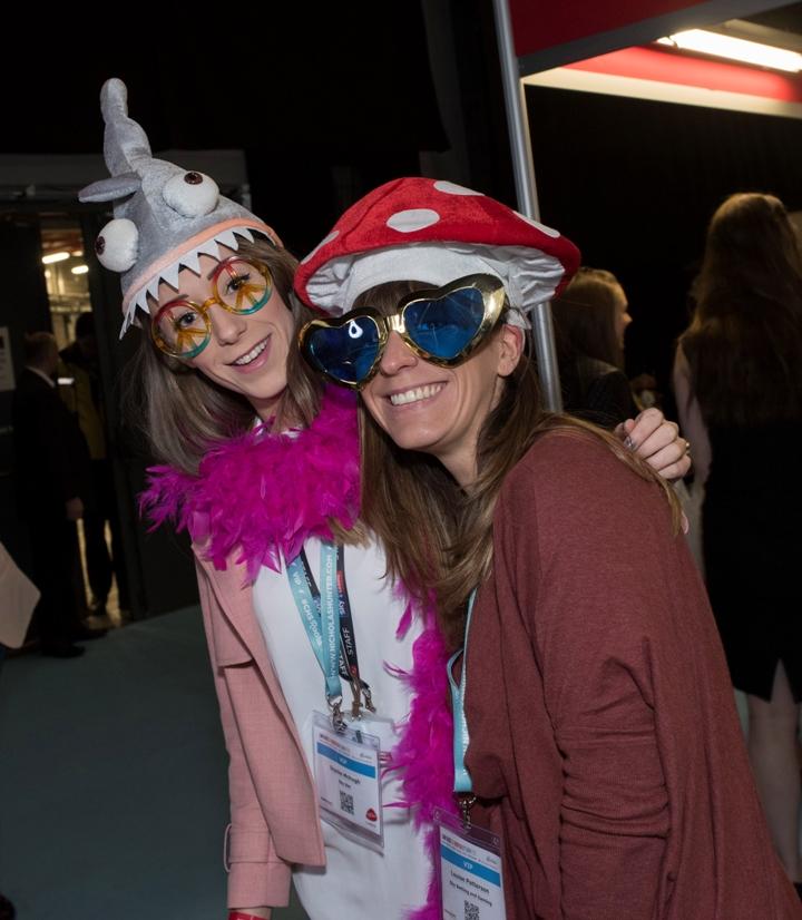 2 ladies dressed in costume; one with a shark hat and the other in a toadstool hat with love-heart shaped glasses.