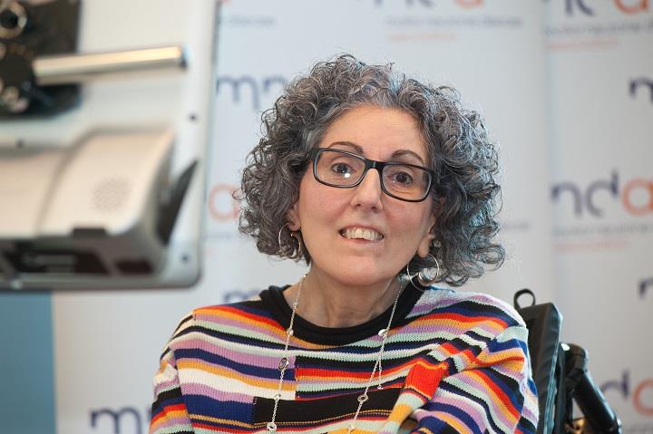 Lady with grey curly hair with glasses and a colourful stripey top.
