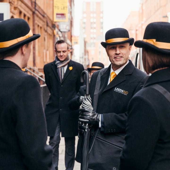3 Leeds Ambassadors in black coats and black bowler hats with yellow ribbon.