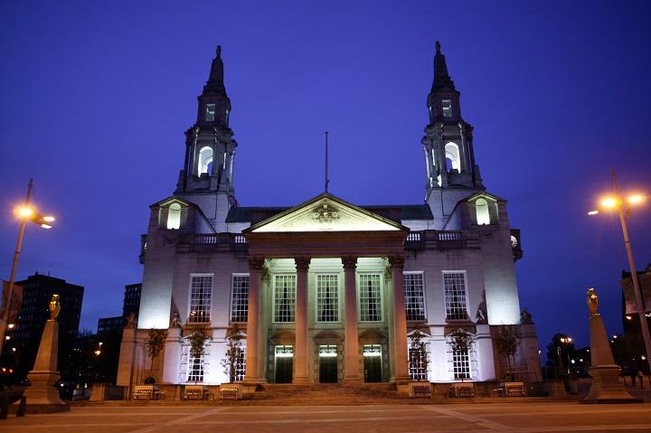 External view of building with 2 towers lit up at night.
