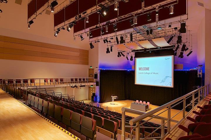 Auditorium with studio lighting with tiered seating facing a projector screen.