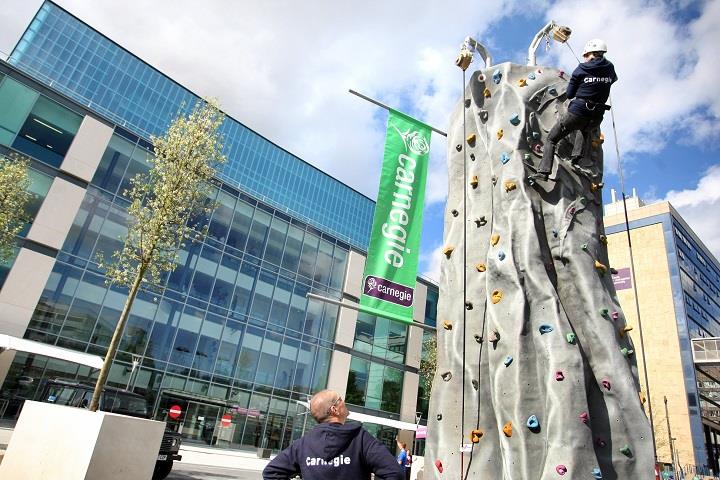 man been watched climbing up a climbing wall outside a glass building.