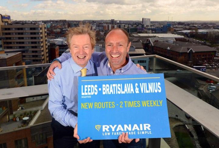 2 men holding a blue sigh on a rooftop with views over Leeds