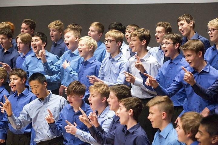 3 rows of boys singing in blue shirts singing