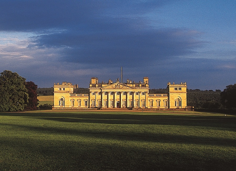 Outside view of Harewood House surrounded by grass and trees with a blue sky