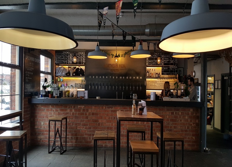 Red brick bar with black worktop. Industrial grey lighting and bar tables to the front,